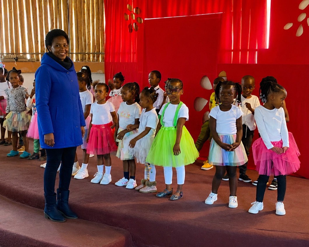A teacher on stage with Zonke Izizwe children in tutus at a school concert