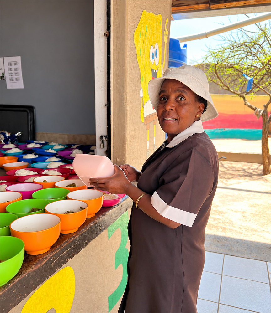 A cook in a sun hat filling rows of coloured bowls with food