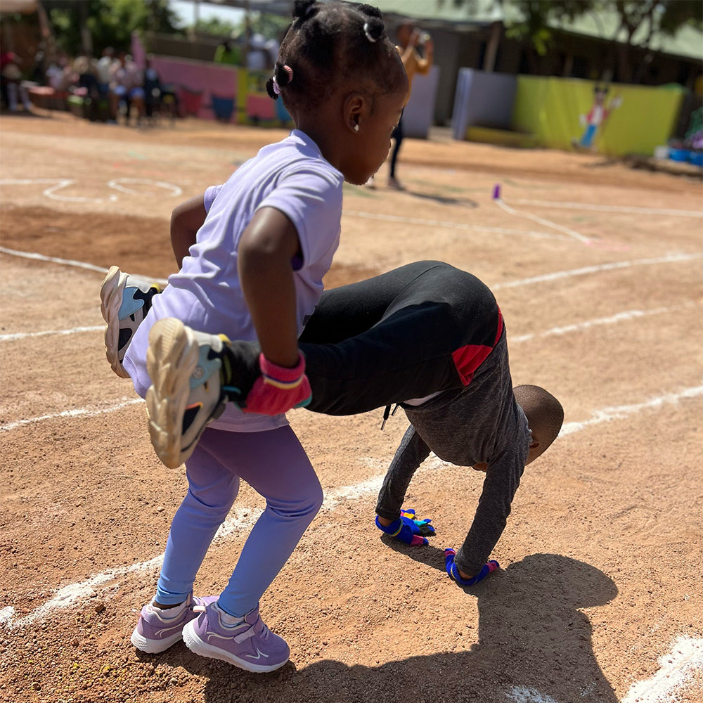 Children doing a wheelbarrow race on the sand track at sports day